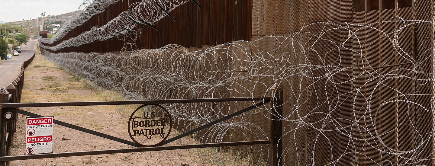 Barbed wire covers a metal fence. A sign says U.S. border patrol.