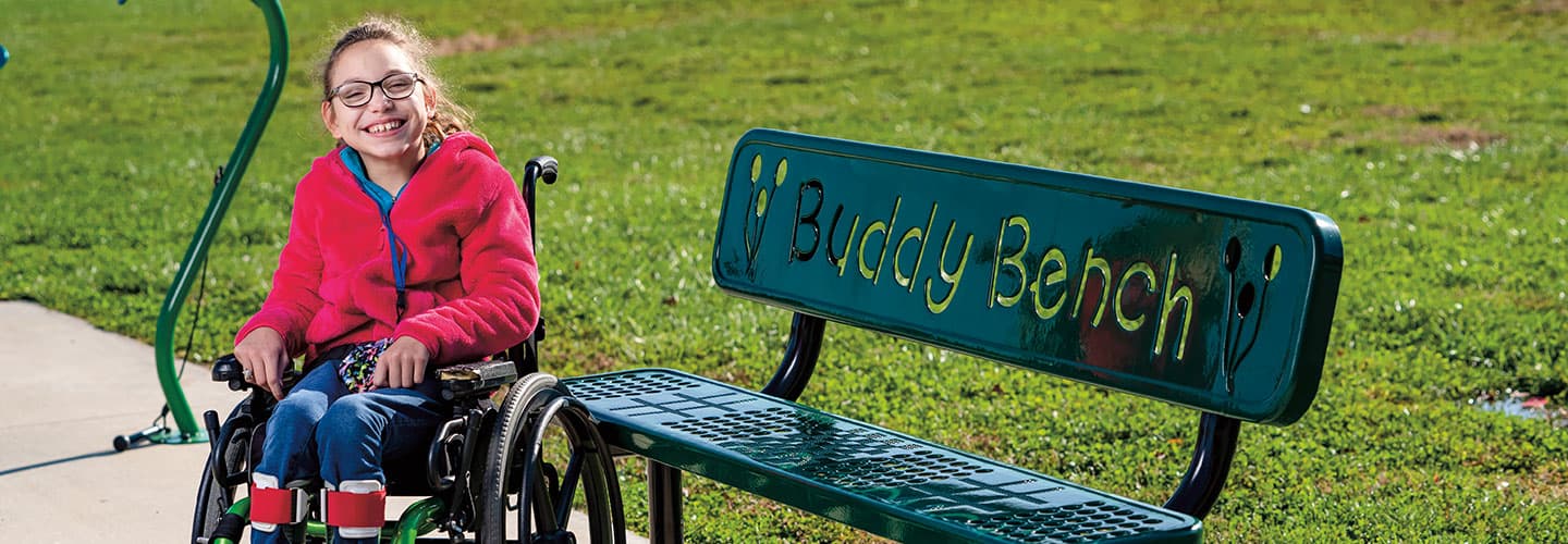 Melody Day smiles in her wheelchair next to a buddy bench