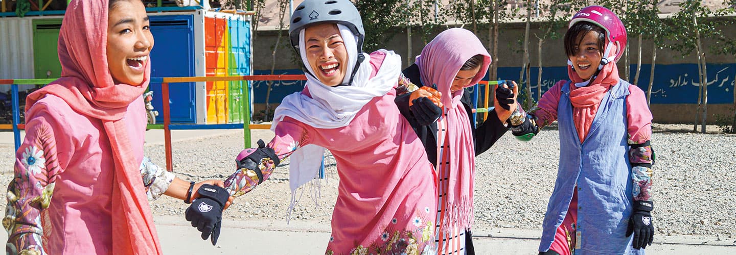 Four young girls wear skating gear and smile in a park