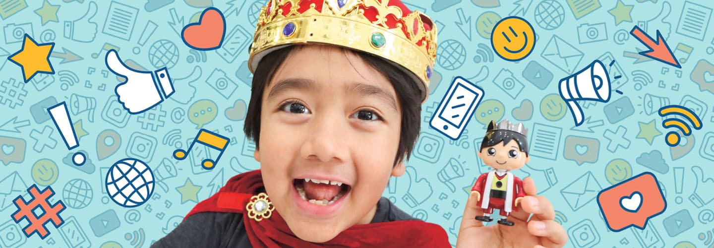 Ryan Kaji smiles and wears a crown while holding a toy figure that looks like him
