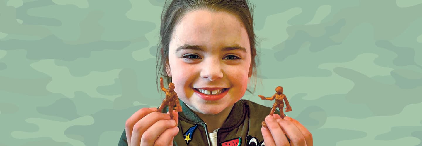 A young girl smiles while holding plastic toy soldiers