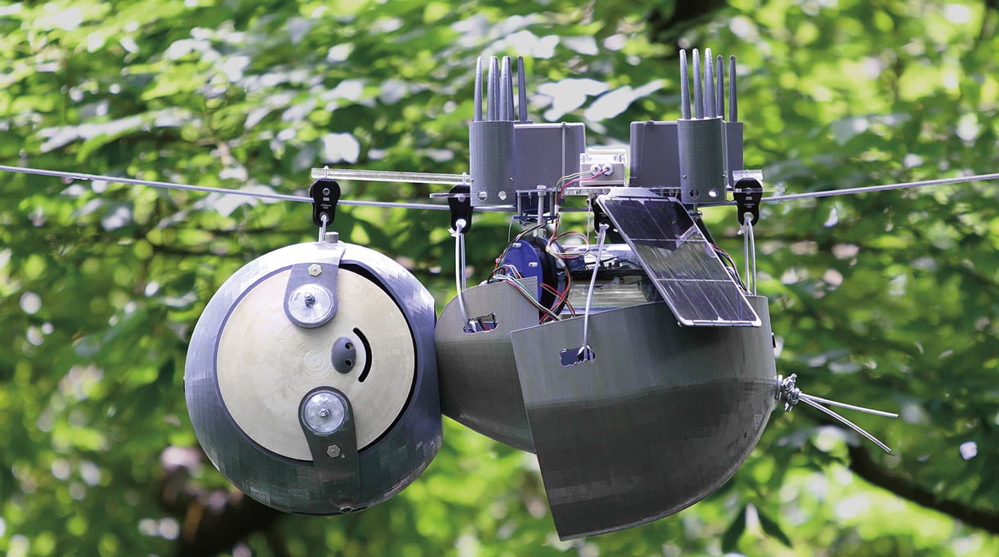 A robot with a smiley face hangs upside down from a wire