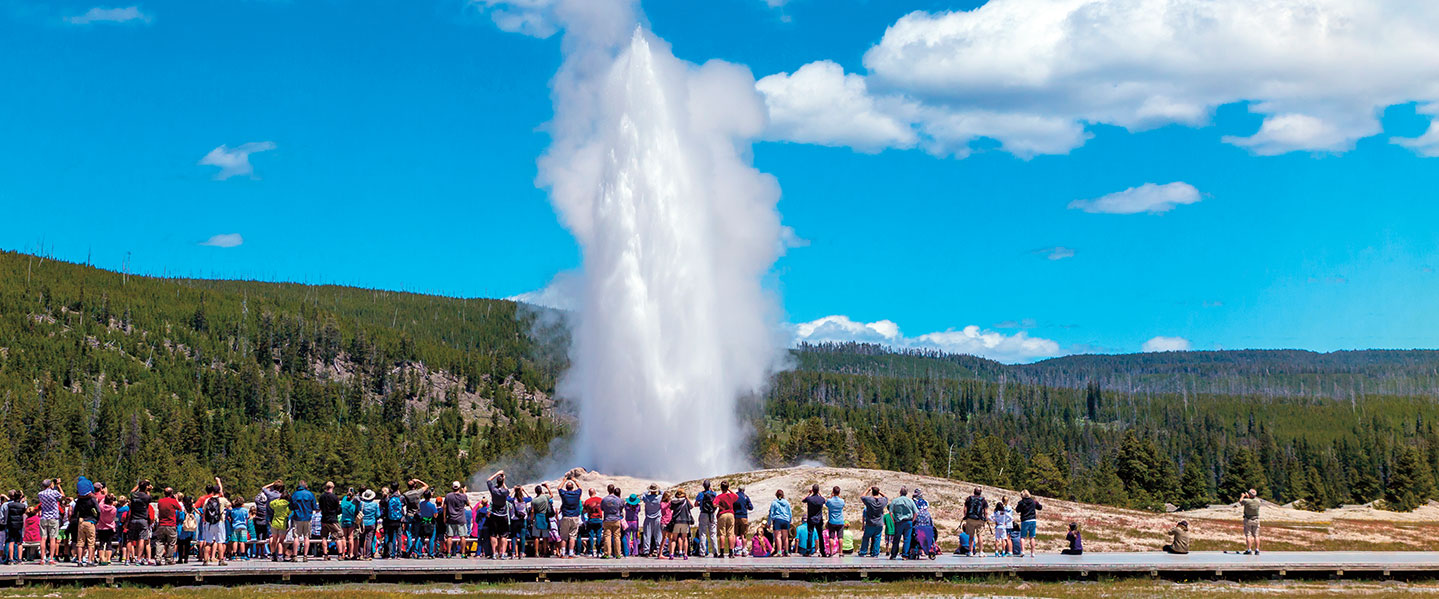 People watch as old faithful shoots water into the air.