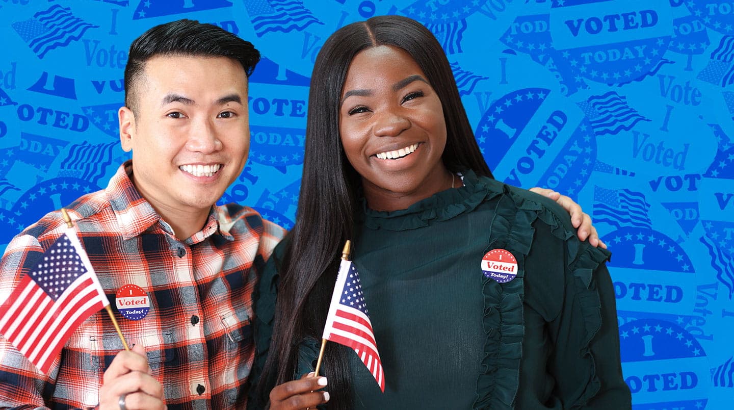 Two people smile while waving flags and wearing I voted stickers.