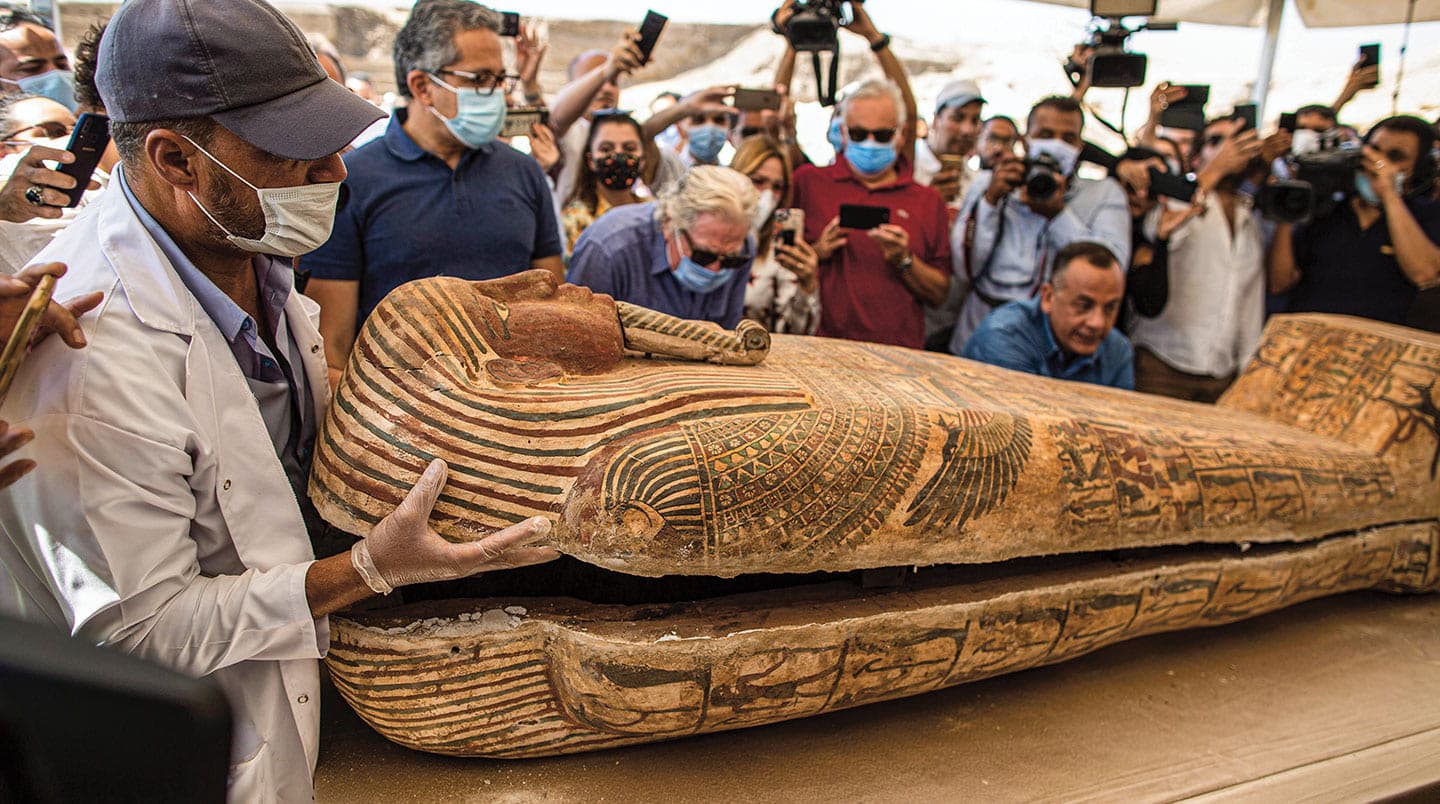 An archaeologist opens a Mummy’s sarcophagus while people take photos