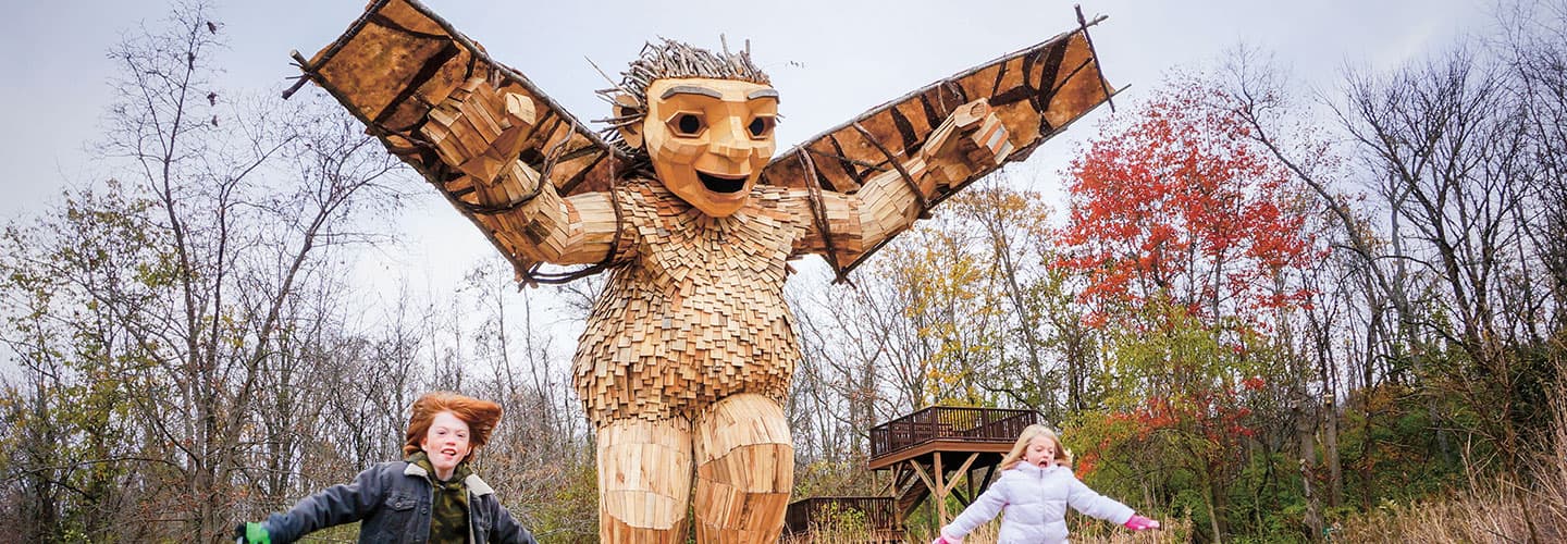 A statue of a large wooden troll holds a pair of wings