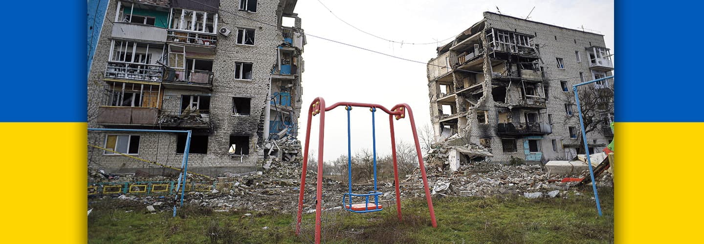 Photo of destroyed apartment buildings and playground with Ukrainian flag in background