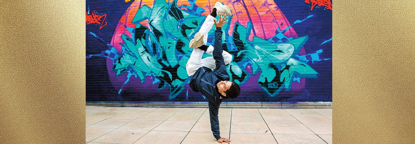 Image of a person break dancing in front of a graffiti wall