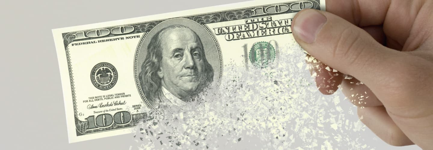 Image of a person holding a one hundred dollar bill in their hand as it is disintegrating