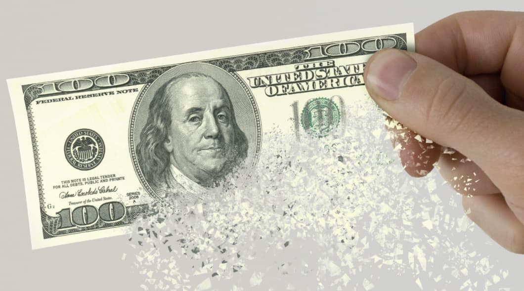 Image of a person holding a one hundred dollar bill in their hand as it is disintegrating