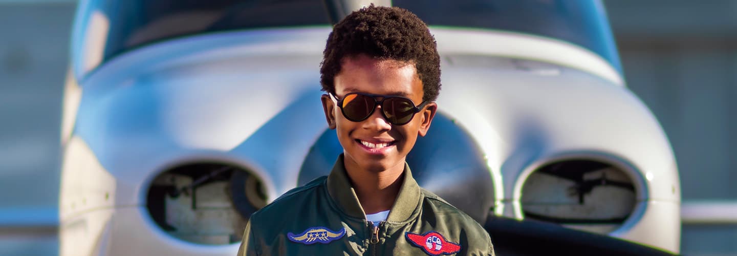 Image of kid wearing pilot gear while standing in front of plane