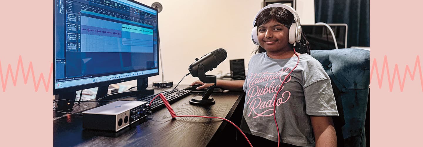 A girl wearing headphones sits at a desk with audio editing software and a microphone
