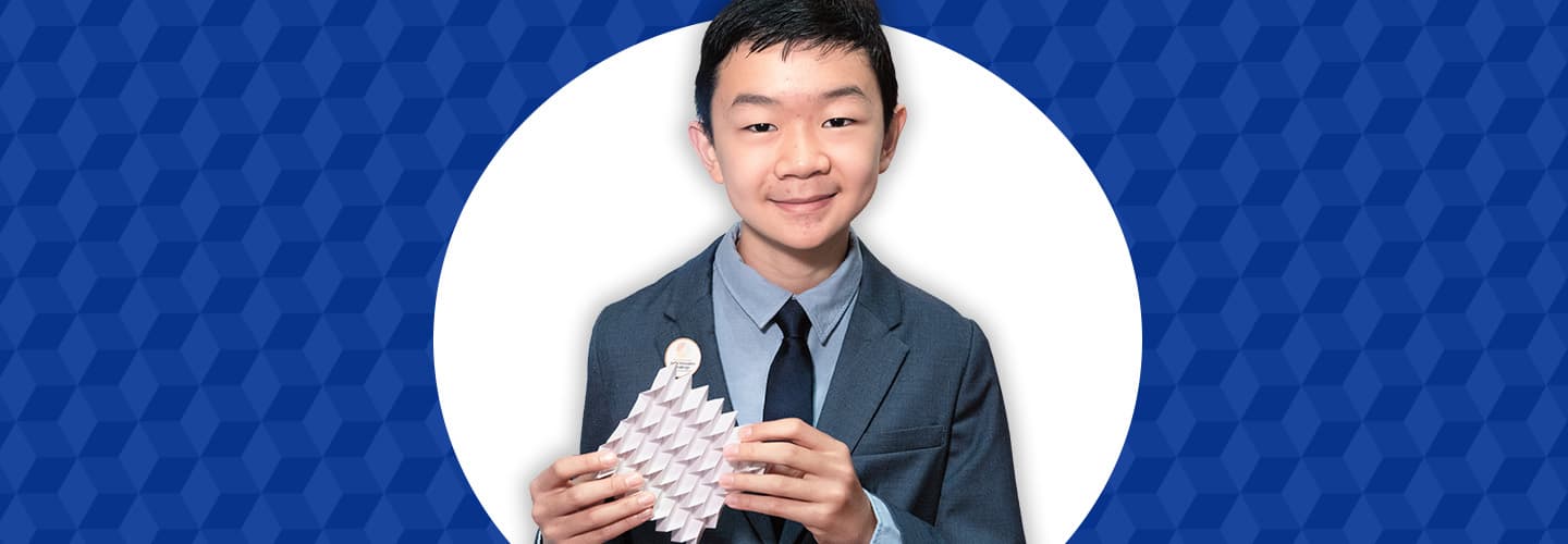 A boy in a suit and tie holds a white paper sculpture with a geometric pattern