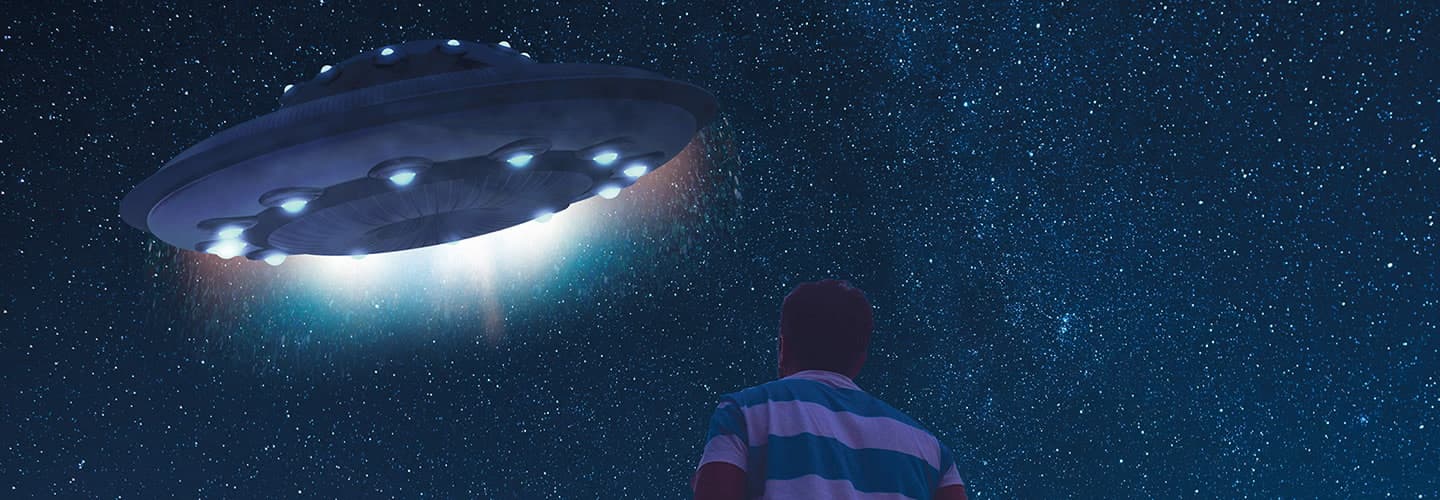 A person looks up at a large lit flying saucer against a star-filled night sky