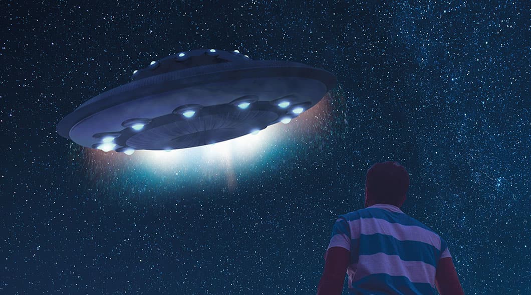 A man looks up at a large glowing UFO against a star-filled night sky